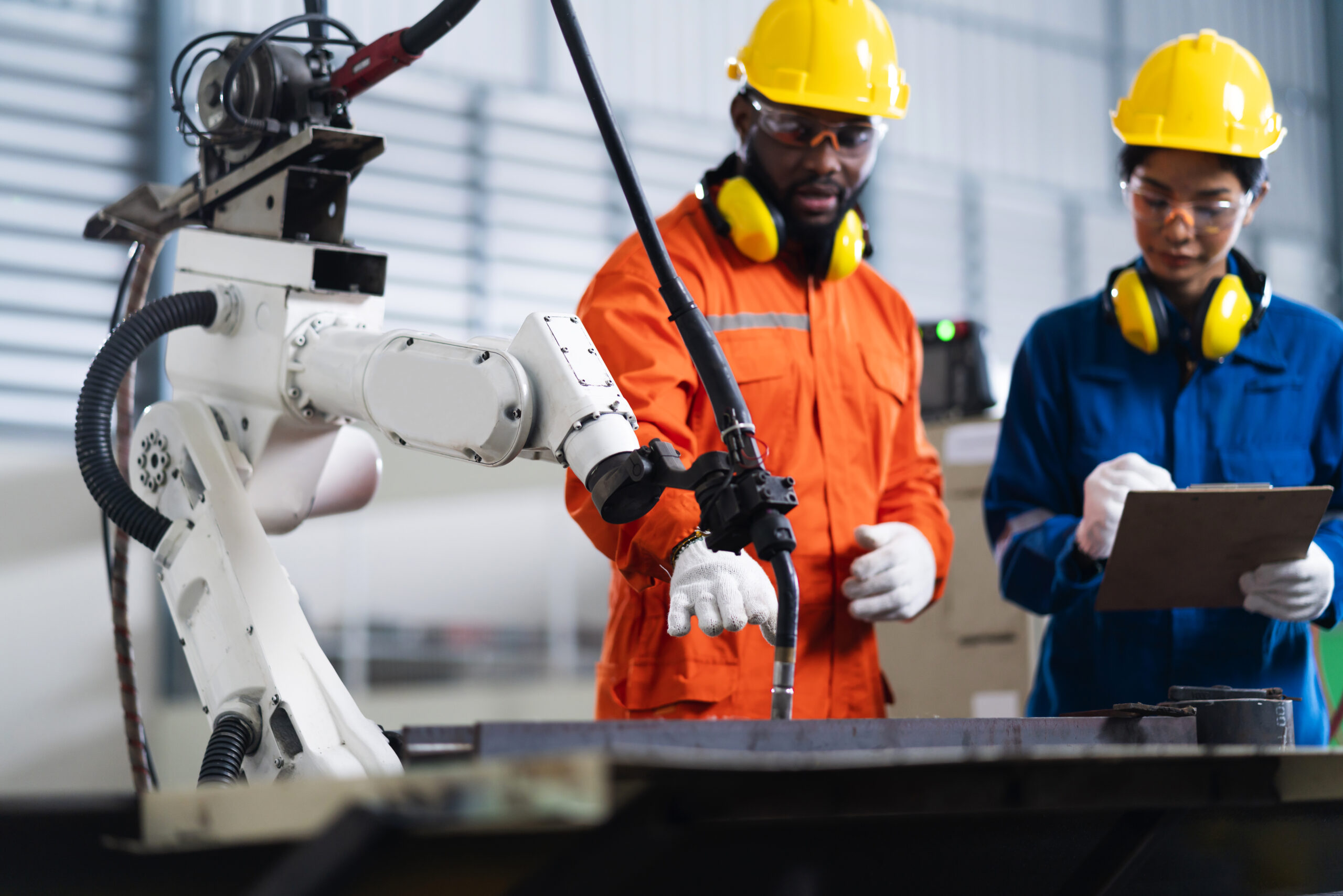 engineer cooperation male and female technician maintenance control relay robot arm system welding with tablet laptop to control quality operate process work heavy industry 4.0 manufacturing factory