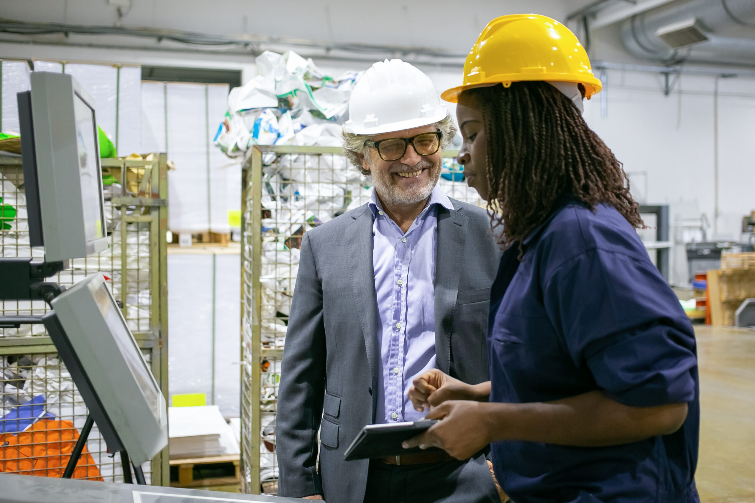 Female factory worker and male engineer talking on plant floor while black woman with tablet operating machine. Low angle. Production process or machinery concept